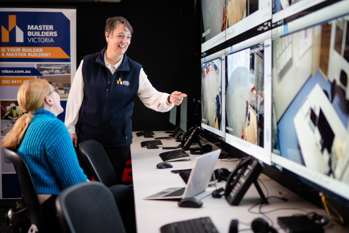 woman wearing a vest with master builders logo showing a young woman something on computer monitors