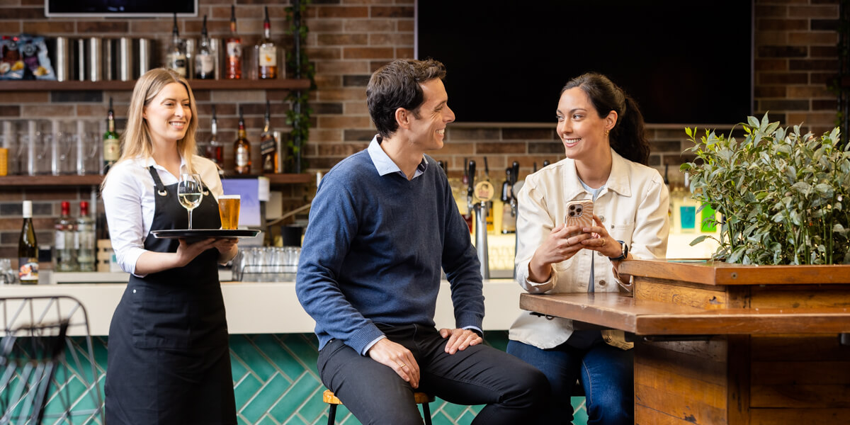 woman bringing a tray of drinks to couple at bar