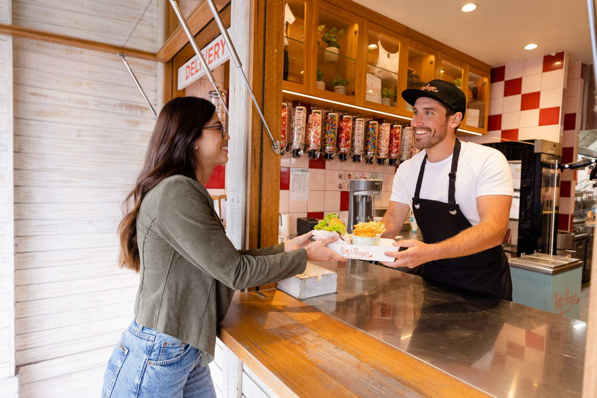 male server handing tray of burgers and chips to young female customer