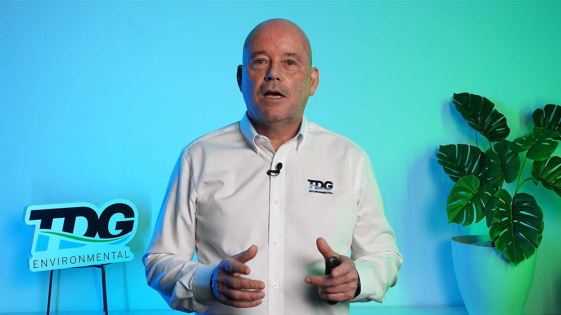 man in white business shirt talking and gesturing with his hands in front of background with a blue green gradient