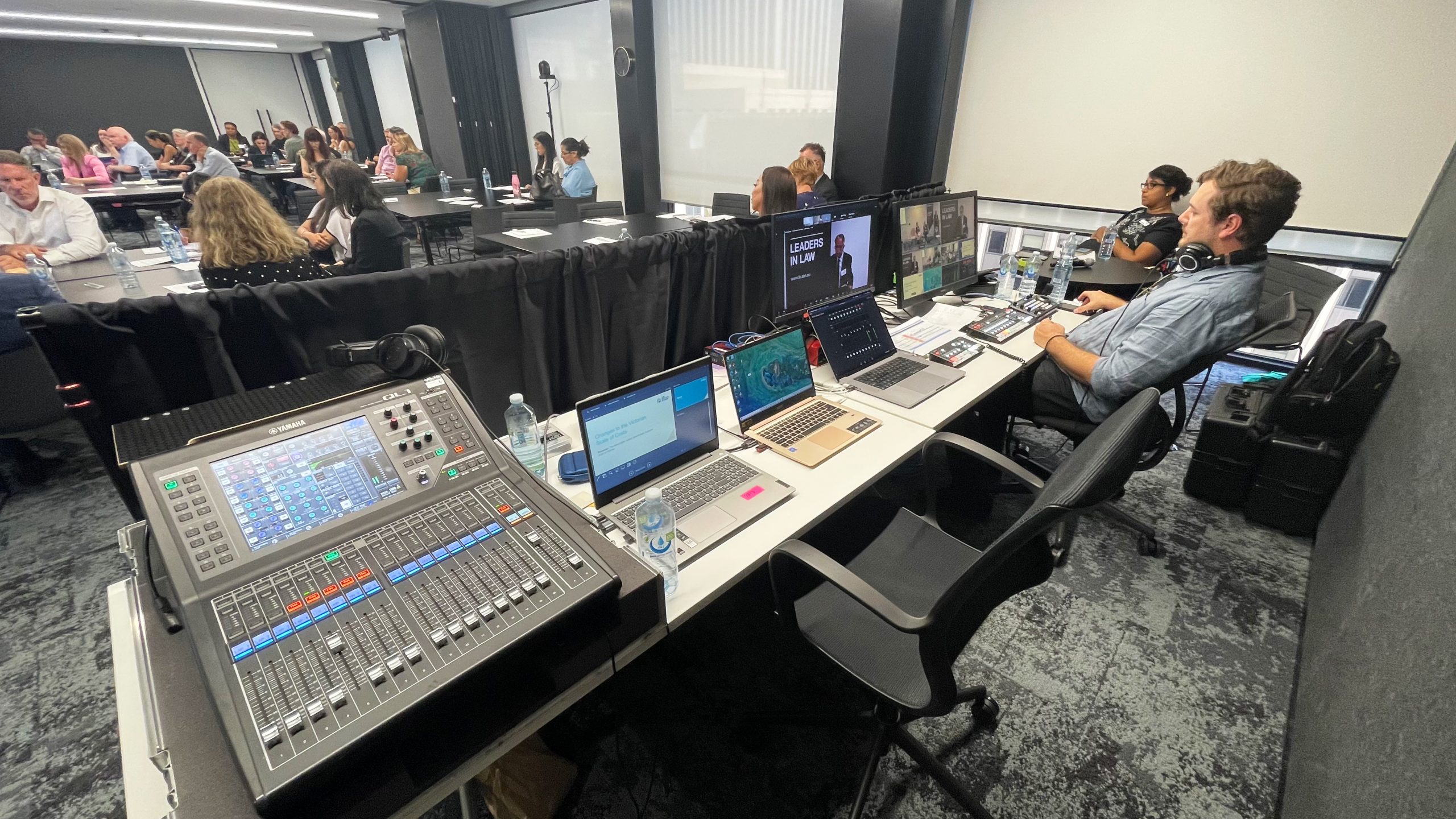 Tech operator sitting behind desk with 3 macbooks, two monitors 