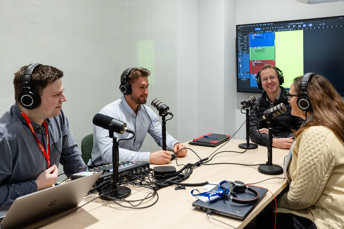 Four adults sitting around boardroom table with earphones on and talking into mics