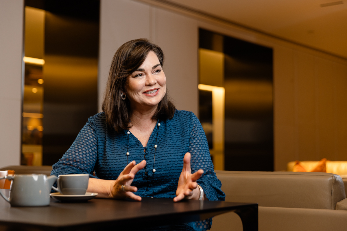 Woman sitting at a desk next to a cup of coffee, gesturing with her hands as she speaks